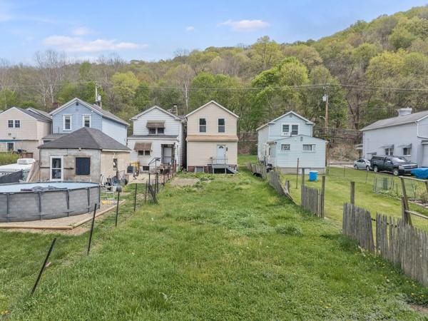 back of house with fence, a lawn, a forest view, and a fenced in pool