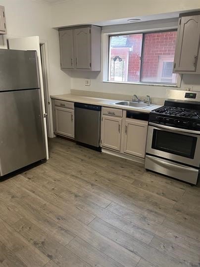 7310 Church St, Swissvale, PA 15218 - kitchen featuring a sink, light wood-style floors, appliances with stainless steel finishes, ornamental molding, and gray cabinetry