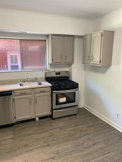 7310 Church St, Swissvale, PA 15218 - kitchen featuring light countertops, wood finished floors, ornamental molding, a sink, and appliances with stainless steel finishes