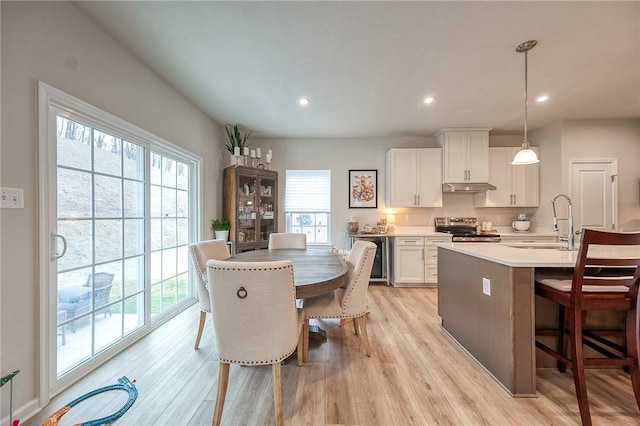 kitchen with a sink, under cabinet range hood, a healthy amount of sunlight, a breakfast bar, and stainless steel electric stove