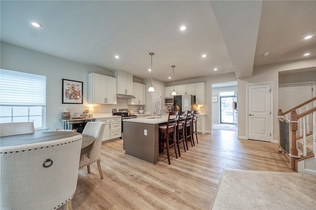 kitchen featuring stainless steel appliances, a sink, light wood-type flooring, an island with sink, and a breakfast bar area