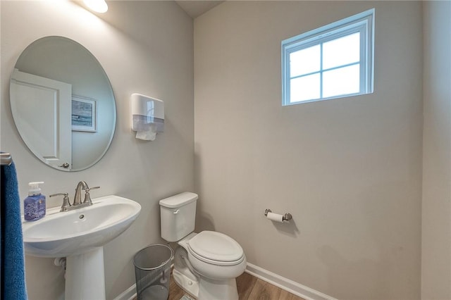 half bathroom with wood finished floors, toilet, baseboards, and a sink