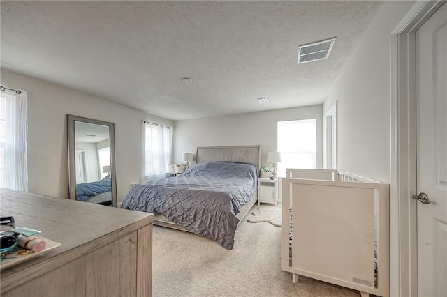 bedroom featuring a textured ceiling, visible vents, and light colored carpet