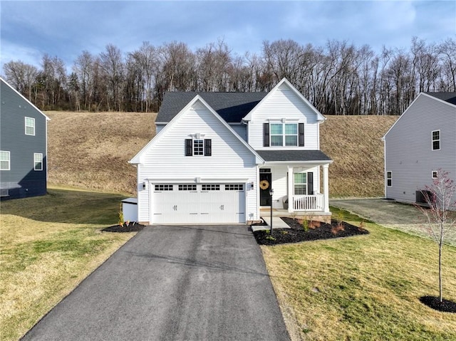 traditional-style house featuring cooling unit, covered porch, an attached garage, a front yard, and aphalt driveway