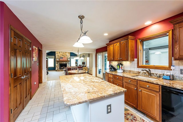 kitchen with light stone counters, a stone fireplace, a sink, black dishwasher, and a kitchen island