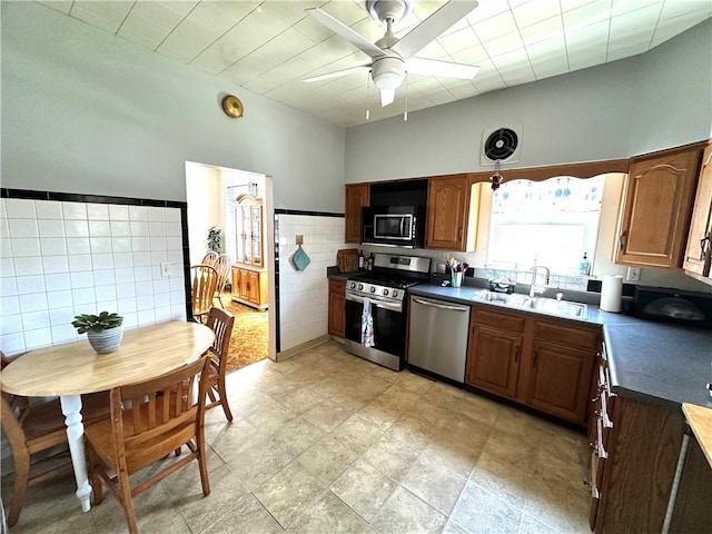 kitchen featuring stainless steel appliances, dark countertops, a sink, tile walls, and ceiling fan