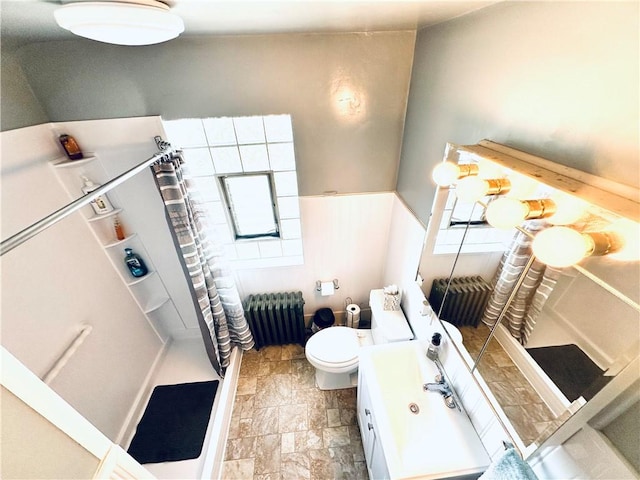 full bathroom featuring stone finish flooring, radiator, toilet, vanity, and a stall shower