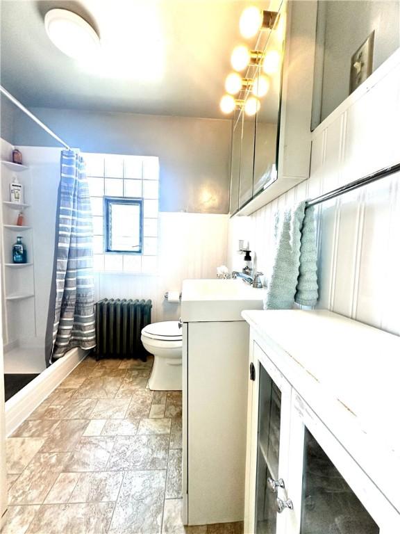 full bathroom featuring stone finish flooring, radiator, a shower with shower curtain, toilet, and vanity