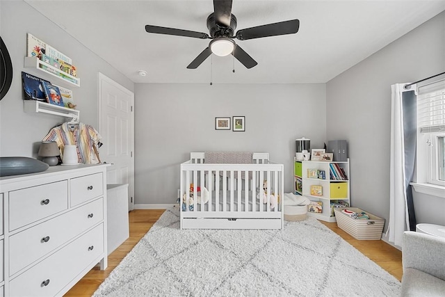 bedroom featuring ceiling fan, a crib, and light wood-style flooring