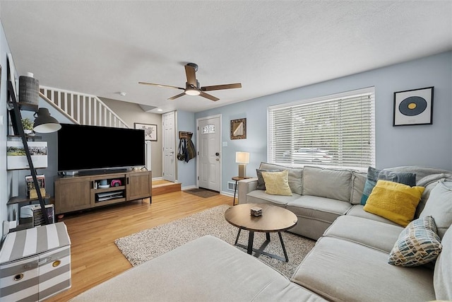living room featuring baseboards, a ceiling fan, stairs, and light wood-type flooring