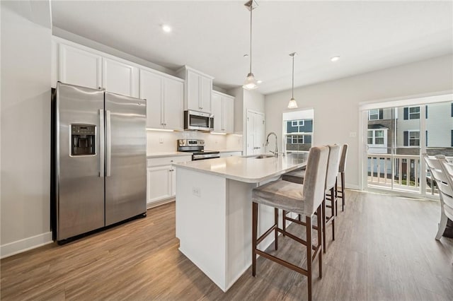 kitchen with light wood finished floors, stainless steel appliances, a kitchen island with sink, and white cabinets