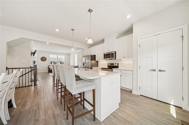 kitchen with light wood-style floors, white cabinetry, appliances with stainless steel finishes, and a large island with sink