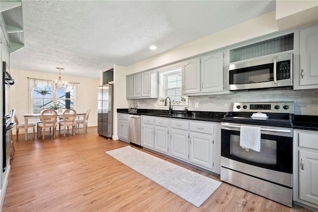 kitchen with stainless steel appliances, backsplash, dark countertops, light wood-type flooring, and a chandelier