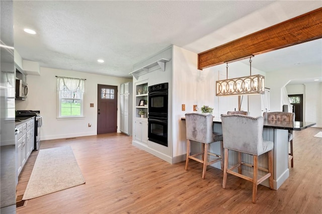 kitchen featuring recessed lighting, stainless steel appliances, a breakfast bar, light wood-type flooring, and baseboards