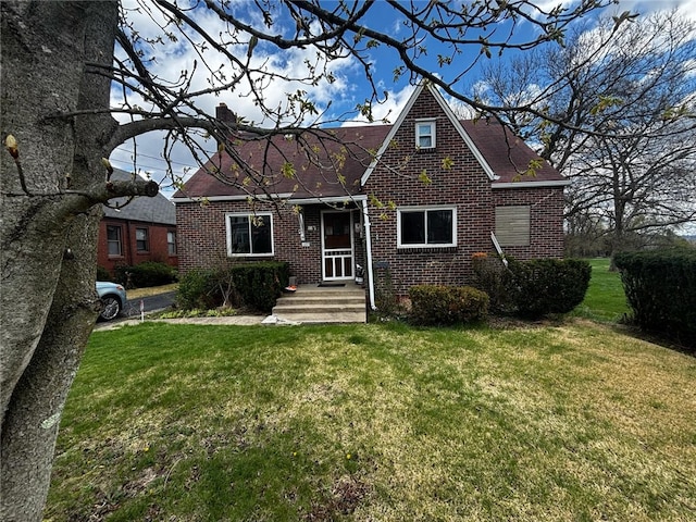 english style home featuring a chimney, a front lawn, brick siding, and roof with shingles
