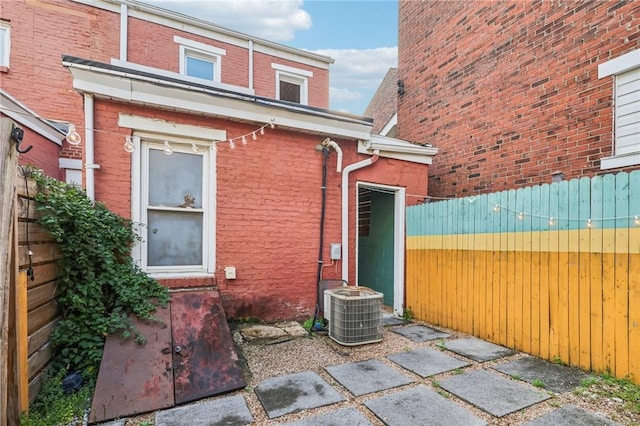 view of side of property featuring cooling unit, brick siding, and fence