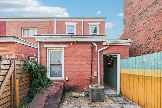 rear view of house featuring fence, brick siding, and central air condition unit