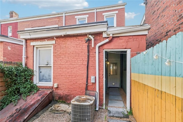 view of exterior entry featuring cooling unit, brick siding, and fence
