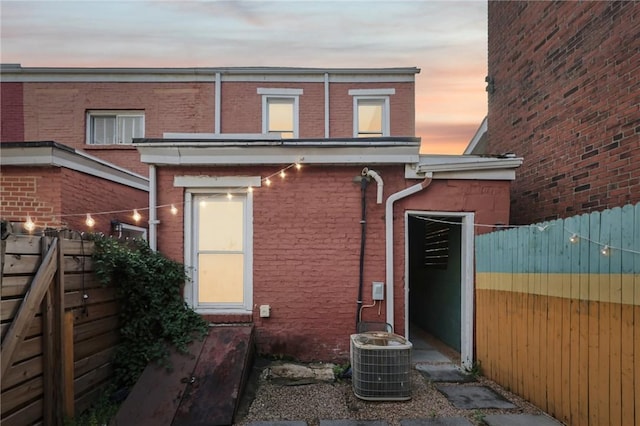 back of house at dusk featuring brick siding, central AC, and fence