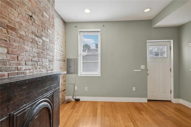 entrance foyer with a fireplace, baseboards, brick wall, and light wood-type flooring