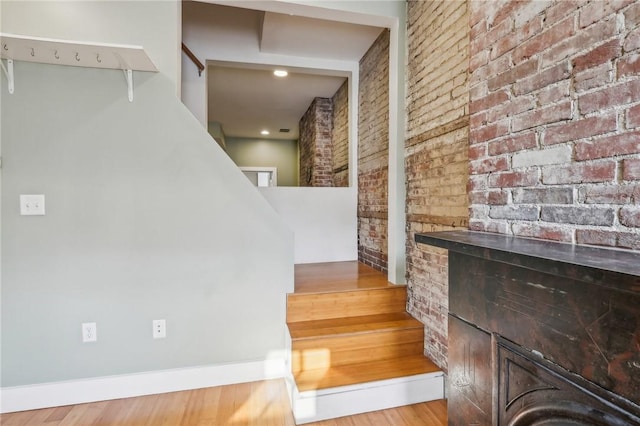 staircase with wood finished floors and brick wall