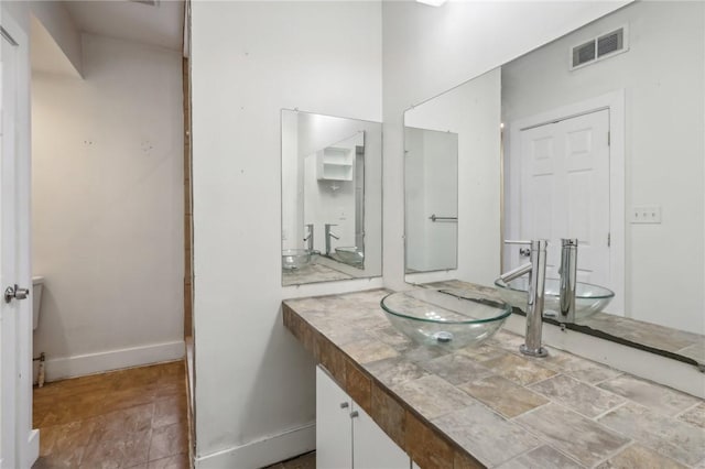 bathroom featuring baseboards, visible vents, stone finish flooring, and vanity