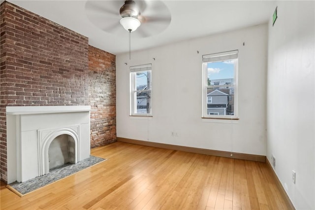 unfurnished living room featuring a large fireplace, hardwood / wood-style floors, a ceiling fan, and baseboards