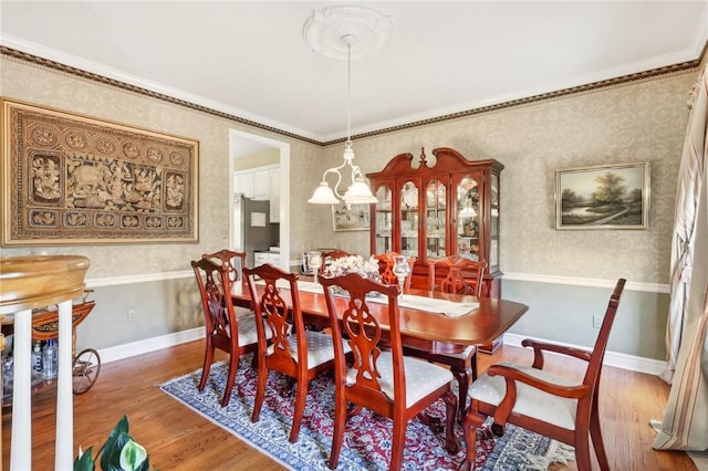 dining space featuring wallpapered walls, ornamental molding, and wood finished floors