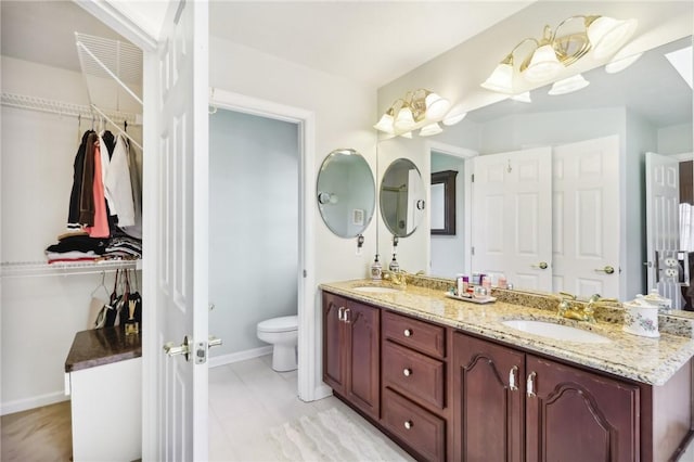 bathroom with double vanity, toilet, a sink, and a walk in closet