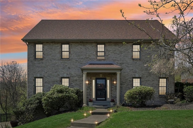 view of front of property with roof with shingles, brick siding, and a front yard