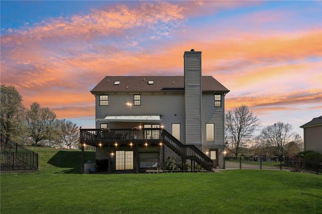 back of property at dusk with fence, stairs, a deck, a chimney, and a yard