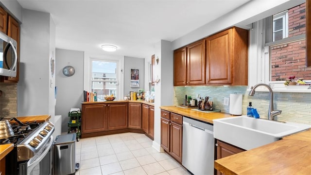 kitchen featuring a sink, wooden counters, decorative backsplash, light tile patterned floors, and appliances with stainless steel finishes