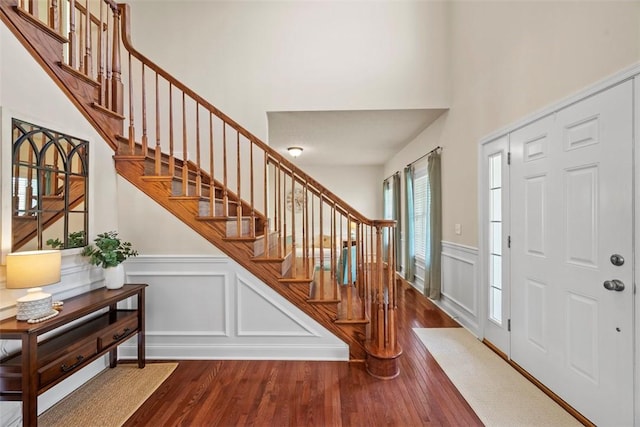 foyer featuring wood finished floors, a decorative wall, stairs, wainscoting, and a towering ceiling