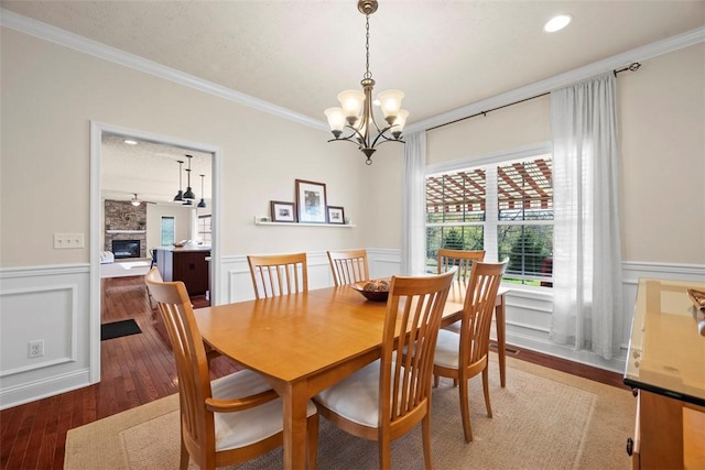 dining space featuring crown molding, wainscoting, a chandelier, a large fireplace, and wood finished floors