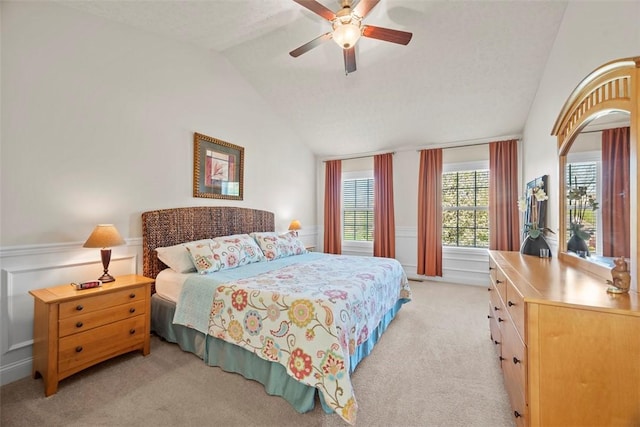 bedroom with lofted ceiling, light colored carpet, wainscoting, a ceiling fan, and a decorative wall