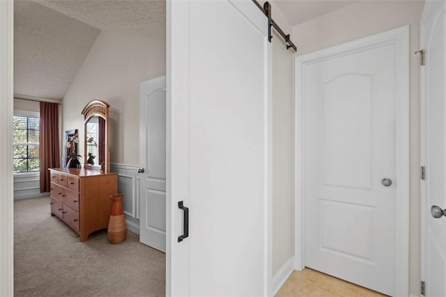 corridor with a barn door, lofted ceiling, light carpet, and a wainscoted wall