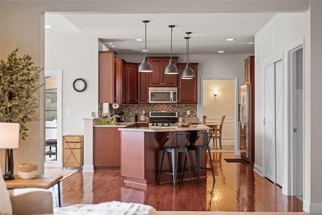 kitchen featuring appliances with stainless steel finishes, dark wood finished floors, tasteful backsplash, a center island, and a breakfast bar