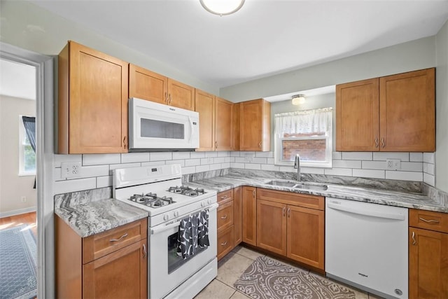 kitchen featuring light stone counters, tasteful backsplash, a sink, and white appliances
