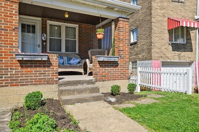 entrance to property with fence, a porch, and brick siding