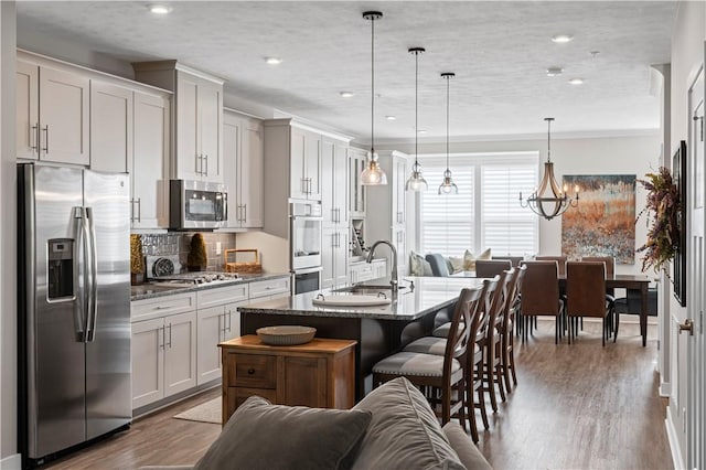 kitchen featuring stainless steel appliances, a sink, wood finished floors, an island with sink, and a breakfast bar area