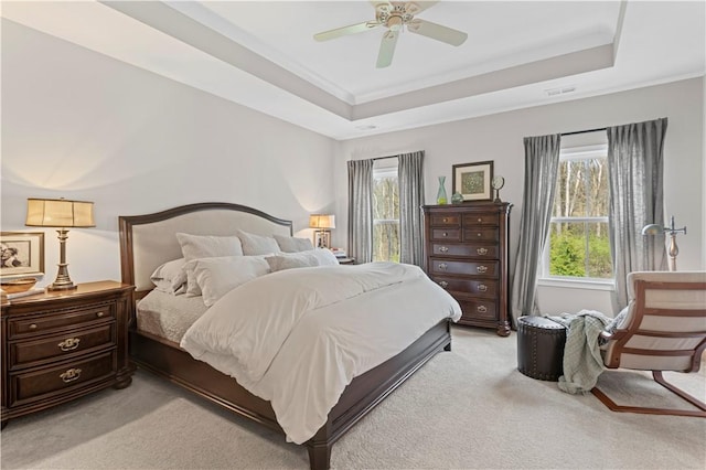 bedroom with crown molding, ceiling fan, a tray ceiling, light colored carpet, and visible vents