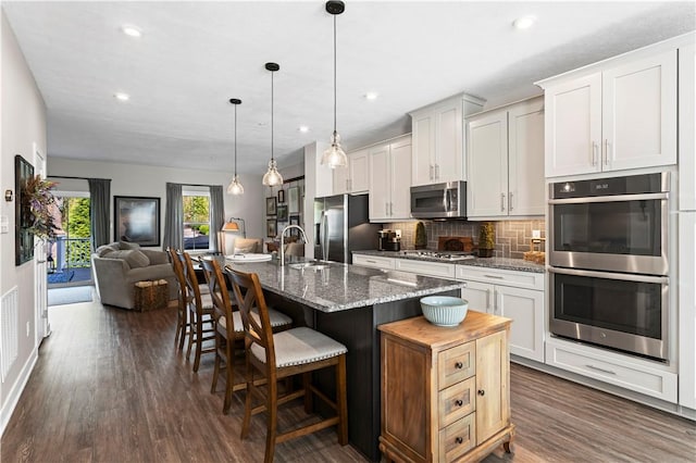 kitchen featuring a kitchen breakfast bar, a sink, tasteful backsplash, dark wood-type flooring, and appliances with stainless steel finishes