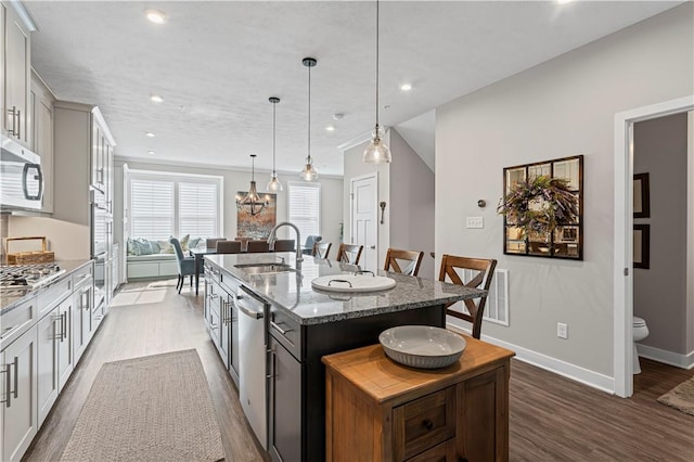 kitchen featuring dark wood-style floors, a sink, appliances with stainless steel finishes, an island with sink, and a breakfast bar area