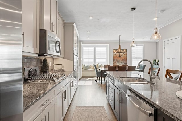 kitchen with stainless steel appliances, light wood-style flooring, a sink, and dark stone countertops