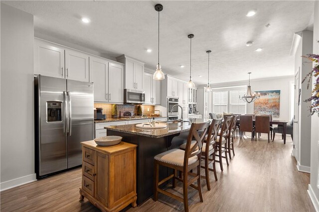kitchen featuring stainless steel appliances, baseboards, decorative backsplash, wood finished floors, and an island with sink