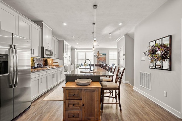 kitchen featuring a center island with sink, visible vents, wood finished floors, appliances with stainless steel finishes, and a breakfast bar area