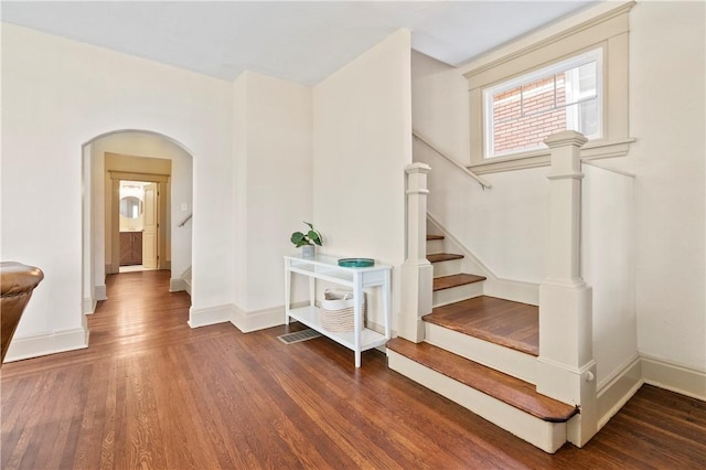 stairway featuring arched walkways, wood finished floors, and baseboards