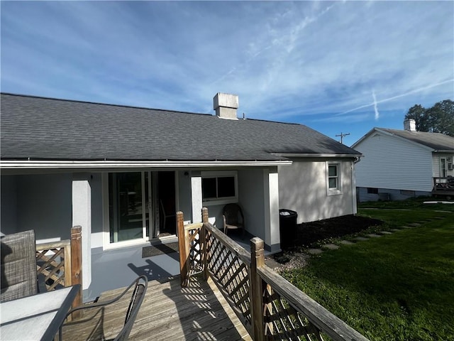 back of property featuring a lawn, a shingled roof, a chimney, and stucco siding