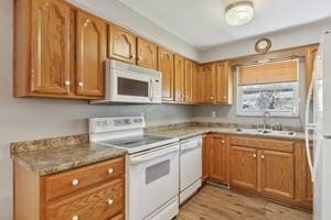 kitchen with brown cabinetry, light wood finished floors, a sink, and white appliances
