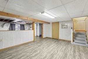 finished below grade area featuring baseboards, a paneled ceiling, stairs, and wood finished floors